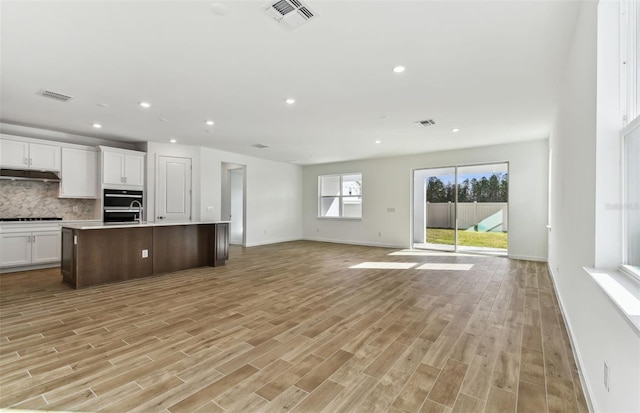 kitchen with tasteful backsplash, a kitchen island with sink, white cabinets, and light hardwood / wood-style floors