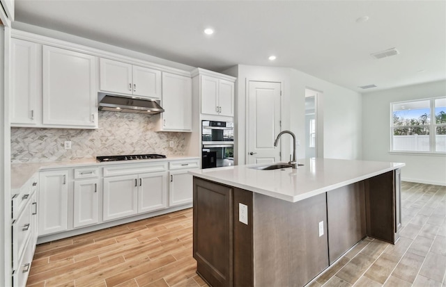 kitchen with a center island with sink, sink, double wall oven, gas stovetop, and white cabinetry