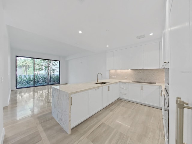 kitchen with sink, kitchen peninsula, backsplash, white cabinetry, and black electric stovetop