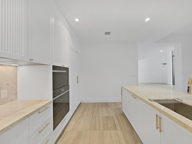 kitchen featuring white cabinets, sink, light stone countertops, and oven