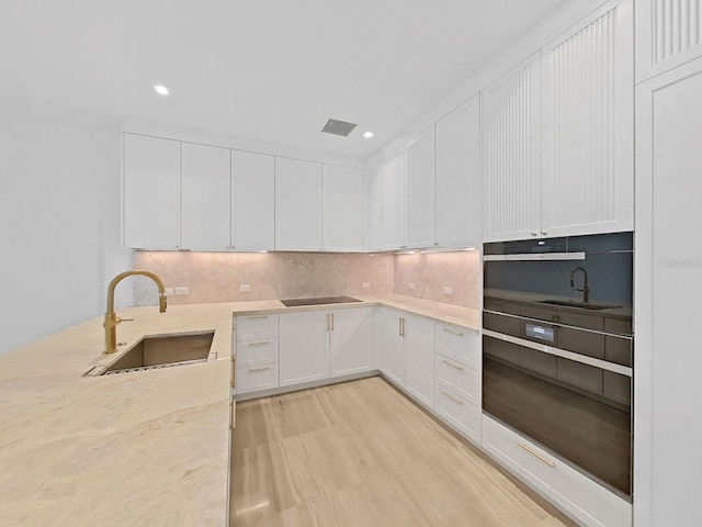 kitchen with black electric stovetop, sink, and white cabinets