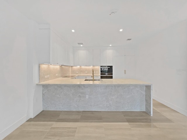 kitchen featuring white cabinets, kitchen peninsula, sink, tasteful backsplash, and black appliances