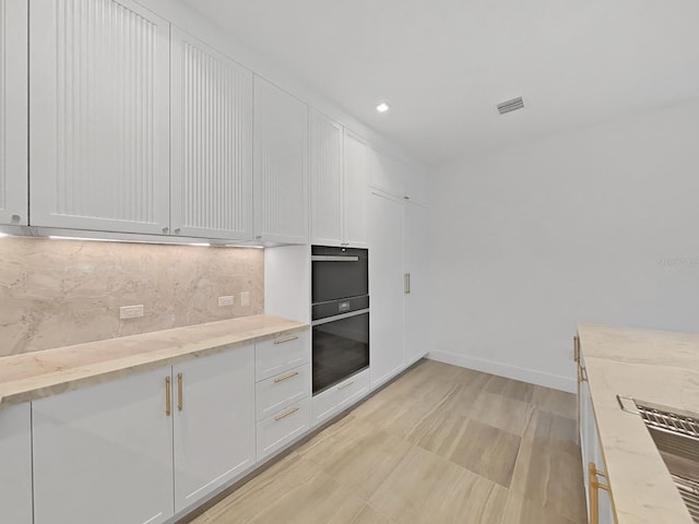 kitchen with white cabinets, black oven, light stone countertops, and tasteful backsplash