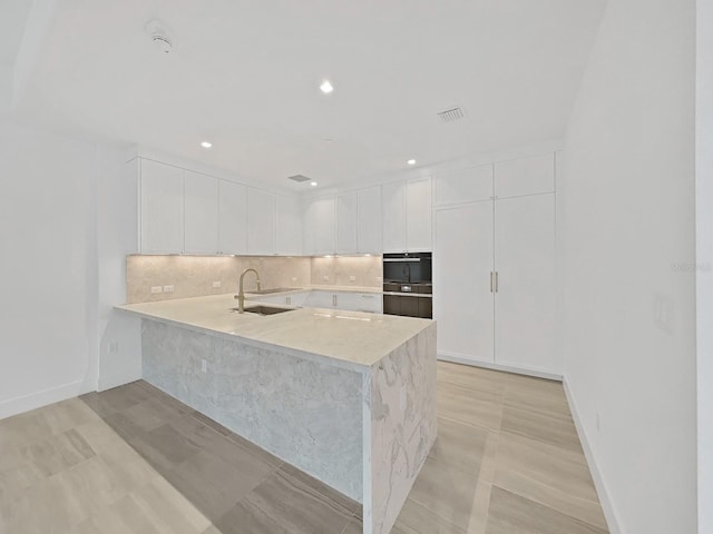 kitchen with white cabinets, backsplash, kitchen peninsula, light tile patterned floors, and sink