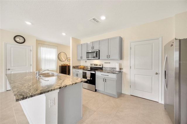 kitchen with dark stone countertops, an island with sink, sink, appliances with stainless steel finishes, and gray cabinetry