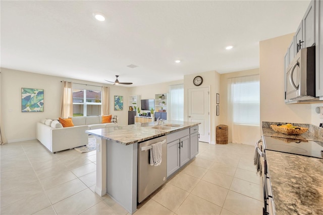 kitchen with a kitchen island with sink, gray cabinets, stainless steel appliances, sink, and ceiling fan