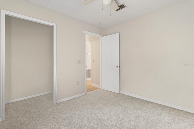 unfurnished bedroom featuring ceiling fan, light colored carpet, and a textured ceiling