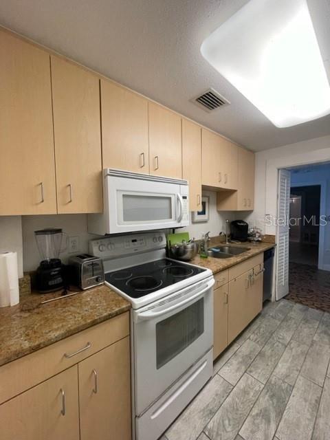 kitchen with light brown cabinets, sink, white appliances, stone counters, and light hardwood / wood-style floors