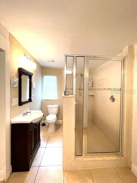 bathroom featuring a shower with shower door, vanity, a textured ceiling, tile patterned flooring, and toilet