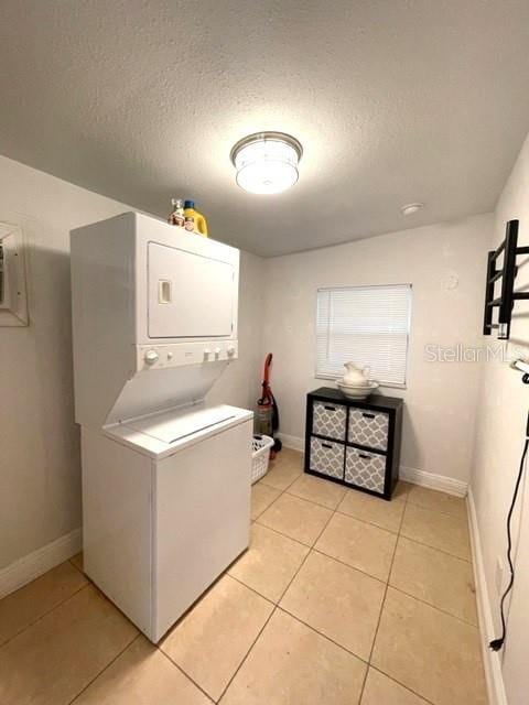 laundry area featuring a textured ceiling, light tile patterned floors, and stacked washer and clothes dryer