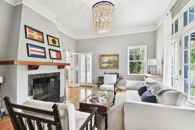 living room with a tiled fireplace, light hardwood / wood-style floors, a notable chandelier, and french doors