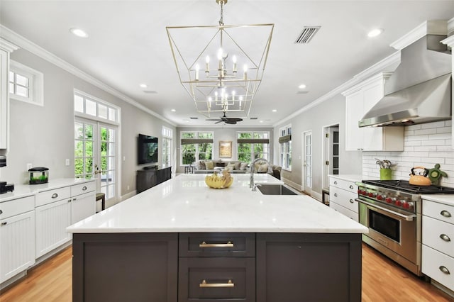 kitchen with pendant lighting, a kitchen island with sink, light hardwood / wood-style floors, sink, and luxury range