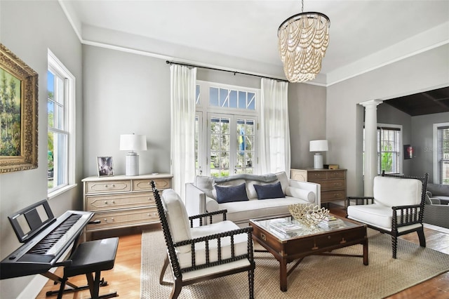 living area with decorative columns, an inviting chandelier, and light hardwood / wood-style flooring