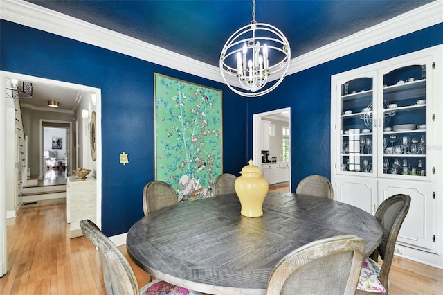 dining area with ornamental molding, an inviting chandelier, and light hardwood / wood-style floors