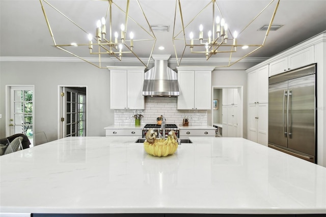 kitchen featuring white cabinets, decorative light fixtures, sink, wall chimney exhaust hood, and stainless steel built in refrigerator