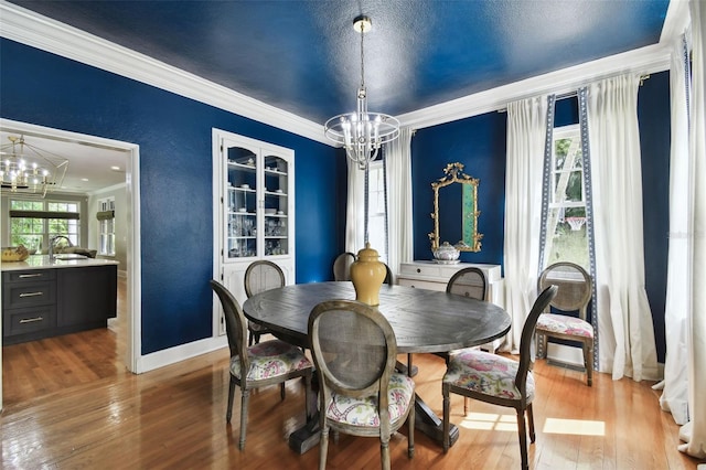 dining space with ornamental molding, a textured ceiling, an inviting chandelier, sink, and light hardwood / wood-style floors