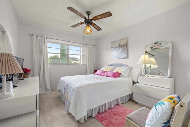 bedroom featuring a textured ceiling, light colored carpet, and ceiling fan