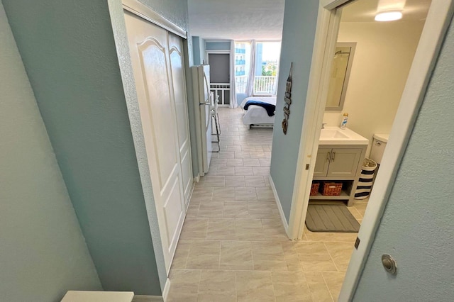 corridor with a textured ceiling, light tile patterned floors, and sink