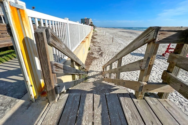 wooden deck featuring a beach view and a water view