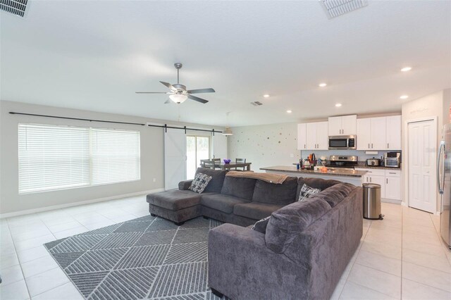 living room featuring a barn door, ceiling fan, and light tile patterned flooring