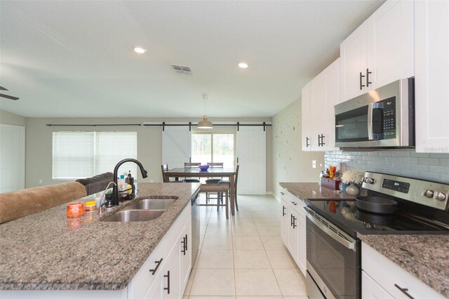 kitchen with appliances with stainless steel finishes, an island with sink, sink, white cabinetry, and a barn door