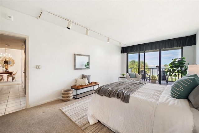 carpeted bedroom featuring a textured ceiling, rail lighting, an inviting chandelier, and access to outside