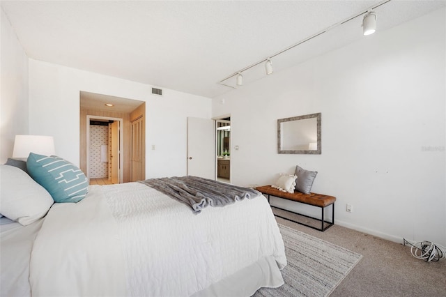 bedroom featuring track lighting, light colored carpet, and ensuite bathroom