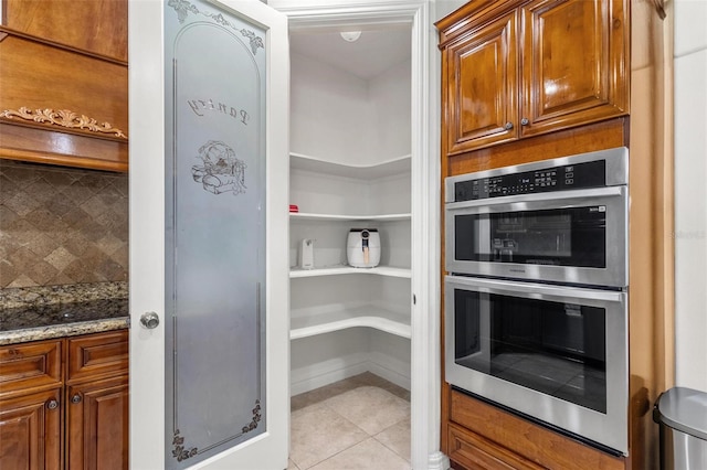 kitchen featuring double oven, light tile patterned floors, decorative backsplash, and stone countertops