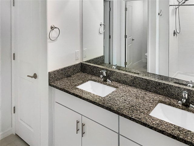 bathroom featuring double vanity, tiled shower, toilet, and a sink