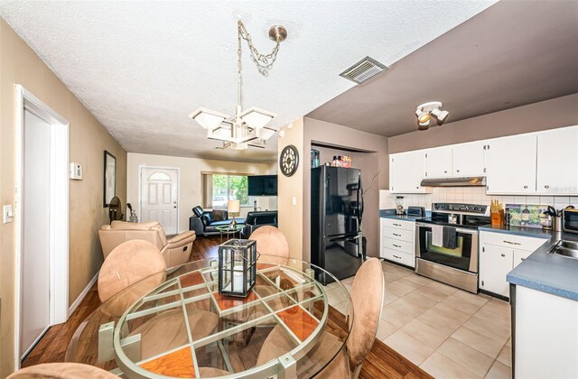 kitchen with stainless steel range with electric stovetop, pendant lighting, white cabinetry, black refrigerator, and light hardwood / wood-style floors