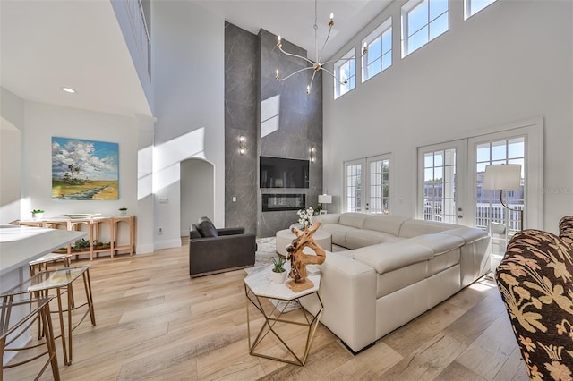 living room with french doors, light hardwood / wood-style flooring, a high end fireplace, and a high ceiling