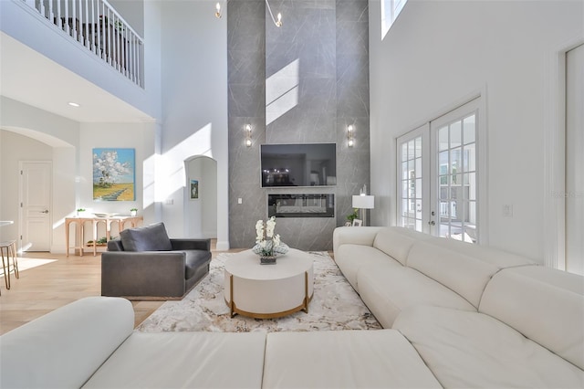 living room featuring a high end fireplace, french doors, a towering ceiling, and light hardwood / wood-style floors