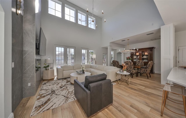 living room with a high ceiling, ceiling fan with notable chandelier, light hardwood / wood-style floors, and french doors