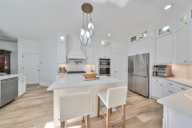 kitchen featuring white cabinetry, a center island, hanging light fixtures, custom range hood, and appliances with stainless steel finishes