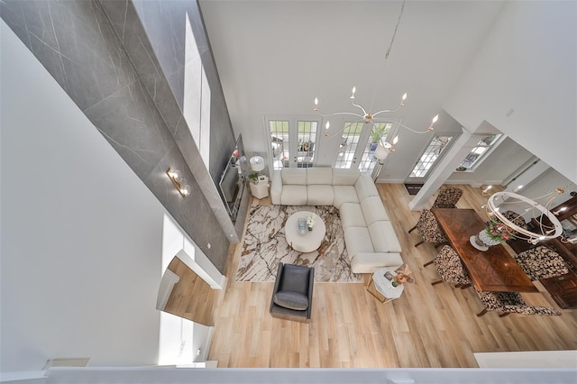 living room featuring french doors, wood-type flooring, a high ceiling, and an inviting chandelier