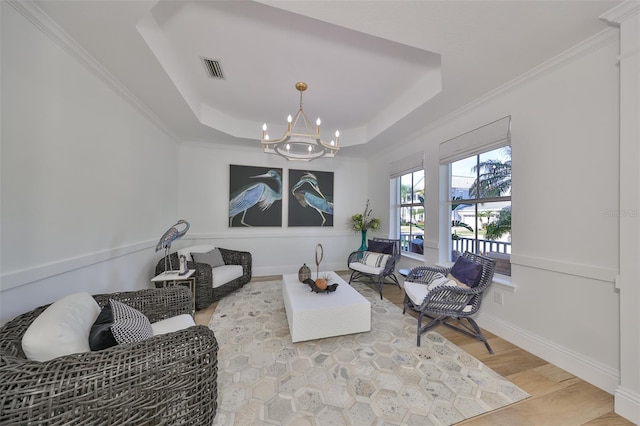 living area with a raised ceiling, light wood-type flooring, and an inviting chandelier