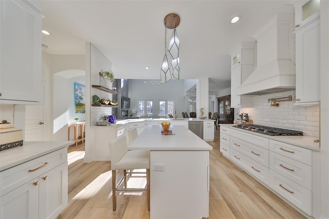 kitchen featuring stainless steel appliances, a peninsula, custom exhaust hood, and light wood-style floors