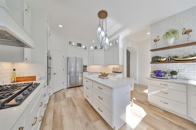 kitchen with light wood finished floors, arched walkways, custom exhaust hood, stainless steel appliances, and light countertops