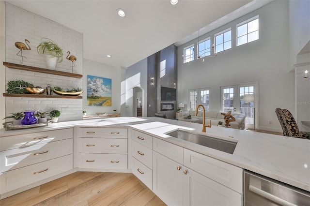 kitchen with light wood-style flooring, white cabinets, a sink, light stone countertops, and dishwasher