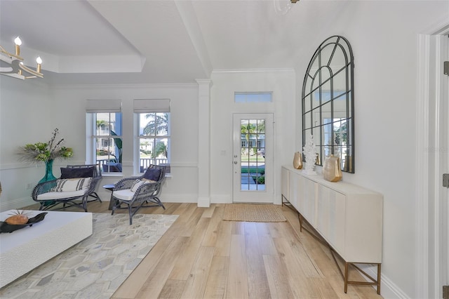 doorway featuring a raised ceiling, baseboards, ornamental molding, light wood-type flooring, and ornate columns