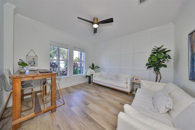 living room featuring ornamental molding, light wood-style floors, a decorative wall, and a ceiling fan