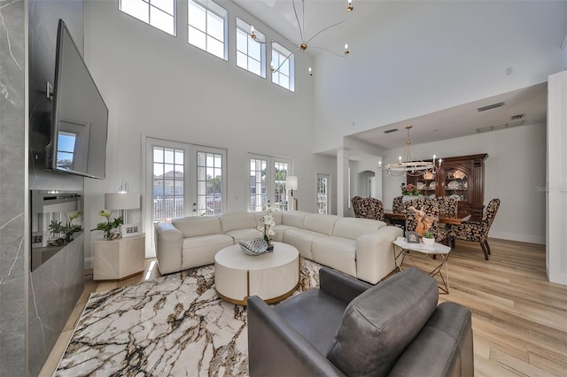 living area featuring french doors, a notable chandelier, ornate columns, wood finished floors, and baseboards