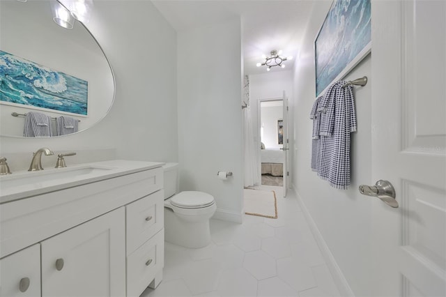 ensuite bathroom with connected bathroom, toilet, vanity, baseboards, and tile patterned floors