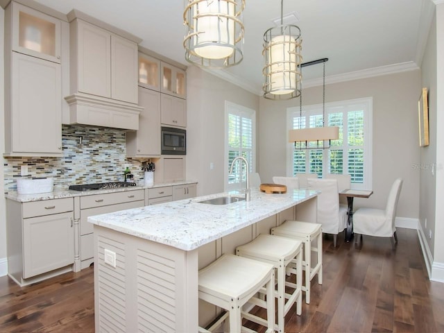 kitchen featuring backsplash, a kitchen island with sink, built in microwave, hanging light fixtures, and sink