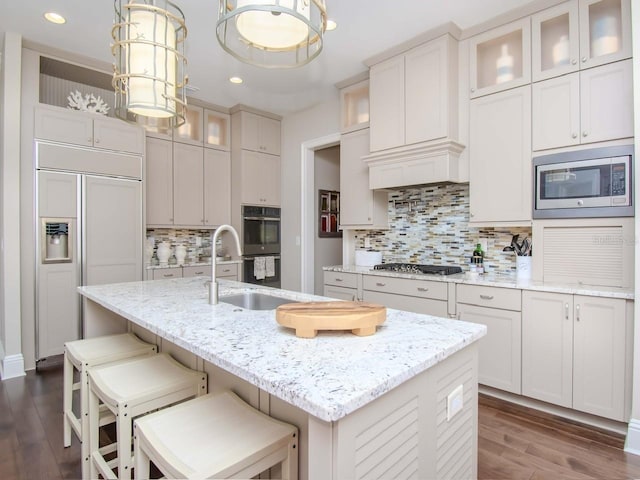 kitchen featuring an island with sink, light stone counters, and built in appliances