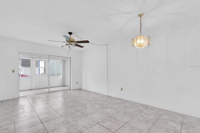 tiled empty room with ceiling fan with notable chandelier and a textured ceiling