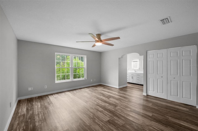 unfurnished bedroom featuring a textured ceiling, ceiling fan, dark hardwood / wood-style flooring, and ensuite bathroom