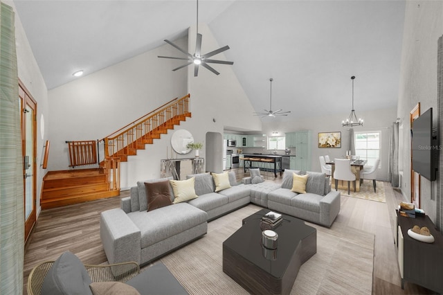 living room with high vaulted ceiling, light hardwood / wood-style floors, and ceiling fan with notable chandelier