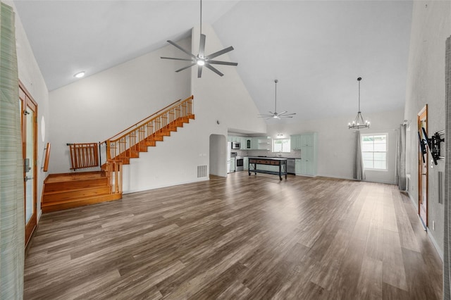 unfurnished living room with hardwood / wood-style flooring, ceiling fan with notable chandelier, and high vaulted ceiling