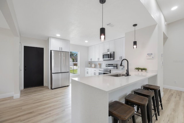 kitchen with appliances with stainless steel finishes, hanging light fixtures, kitchen peninsula, sink, and white cabinetry